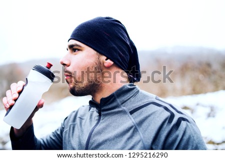 Young Athlete Drinking From Bottle While racing in Trail Run in Winter