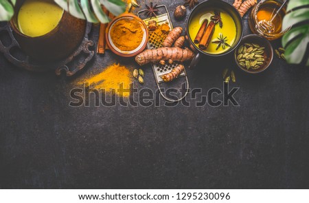 Healthy ingredients border for making turmeric milk drink with fresh turmeric roots , spices and honey on dark background. Hot winter beverage. Immune boosting remedy , detox and dieting concept .  Royalty-Free Stock Photo #1295230096