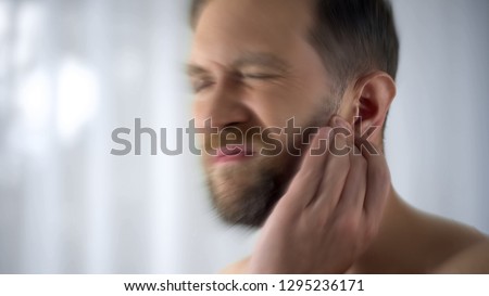 Man holding hurting ear, otitis or infection otolaryngologist problems, close up Royalty-Free Stock Photo #1295236171
