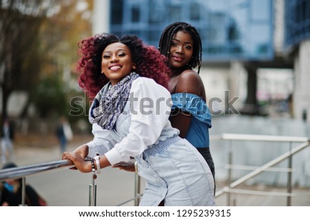 Two attractive african american womans  posed near railings against modern multistory building.