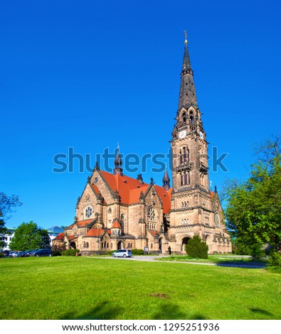 Image of Saint Martin church in Neustadt, Dresden, Germany. Amazing architecture with high towers and red roof. Cloudless spring morning. One cyclist on a bicycle near green lawn and several trees