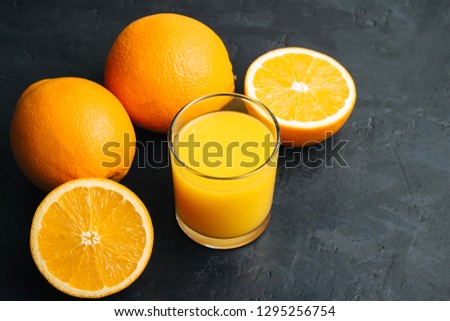 Orange fresh drink, glass of juice and ripe citrus fruits on a black, textured background.