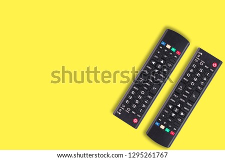 Pair of black plastic remote controls for different multimedia devices on yellow background with copy space for your text. Top view