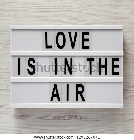 Modern board with text 'Love is in the air' on a white wooden surface. Valentine's Day 14 February.