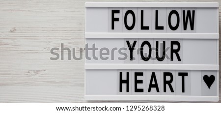 Modern board with text 'Follow your heart' on a white wooden background, overhead view. Flat lay, overhead. Space for text.