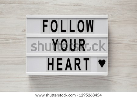 Modern board with text 'Follow your heart' on a white wooden surface, top view. Flat lay, overhead. Valentine's Day 14 February.
