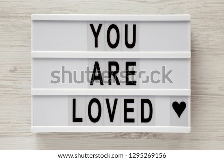 Modern board with text 'You are loved' on a white wooden surface, top view. Flat lay, overhead. Closeup.