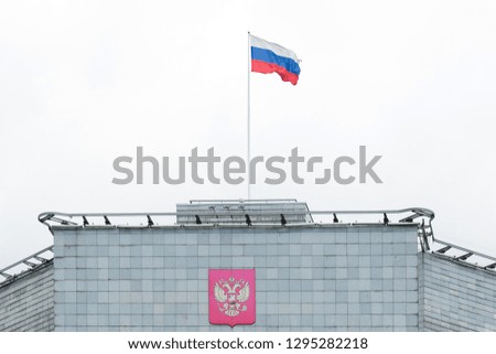 The flag of the Russian Federation develops in the wind on the roof of the government building with the emblem of the country