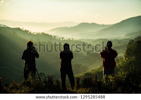 Silhouette of three photographers taking landscape pictures of morning mist on the mountain