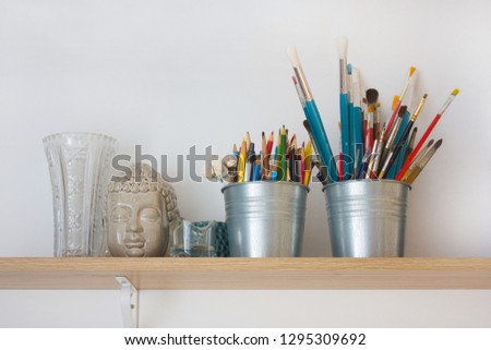 Wooden shelf with pencils, brushes and Buddha head in the artist's studio