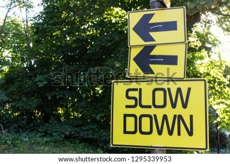 Slow Down yellow road sign green bush at background