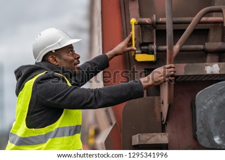 African American railroad engineer wearing safety equipment (helmet and jacket) checking gear train Royalty-Free Stock Photo #1295341996