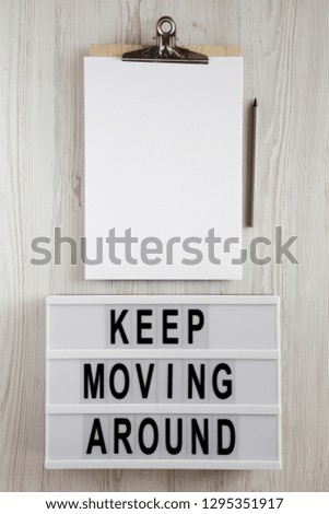'Keep moving around' words on lightbox, clipboard with sheet of paper and pencil on a white wooden surface, top view. From above, flat lay, overhead. 