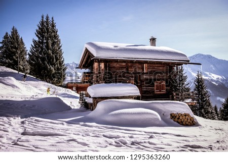 Landscape view of a traditional wooden chalet with its  roofs covered by snow, with snowboarders in the background, in the ski resort of "Verbier", in the "Valais", Switzerland