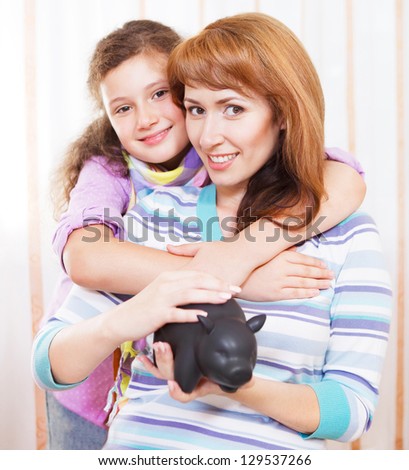 Little girl and mother saving money in a piggybank. Indoor portrait