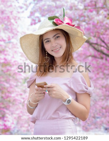 Beautiful Thai woman in pink dress 
 with her sombrero and have pink trumpet tree flower blossom background that very beautiful like sakura blossom field. 