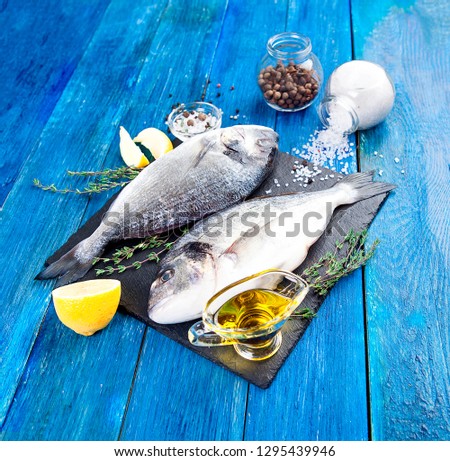 Two ready to cook raw bream fish with herbs, lemon and olive oil on stone slate board. Dorado fish on blue boards. With copy space
