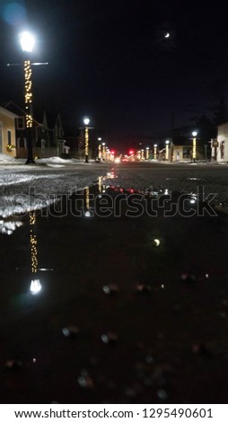 View down a dark street with lights before a puddle reflecting the moon and lights.
