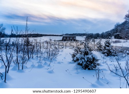 Winter shot over soft white snow to a dam and river on a blue cloudy sunset.