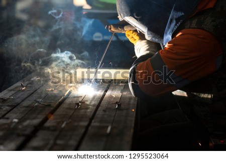The welder is welding with covered electrode to steel material in the workshop.