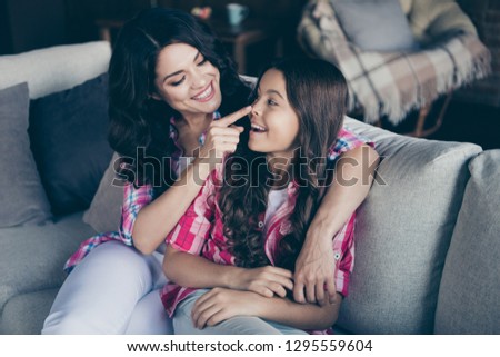 Portrait of two nice gorgeous stylish trendy sweet attractive lovely tender delicate cheerful wavy-haired girls sisters sitting on divan cuddling touching nose indoors