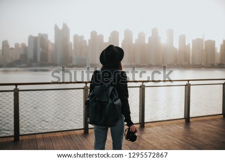 Black hair girl with a camera and bag on the pier on the background of the city