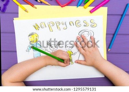 The top view of the child paints a sketch of the family with colored pencils on a white sheet of paper. The word happyness is written on the sheet