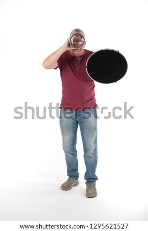 Mature older man in studio holding a beauty photography dish, Photography equipment. casually dressed in jeans and tee shirt. UK White background