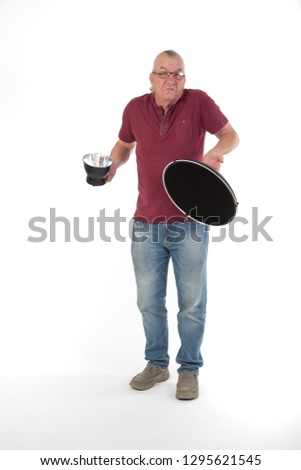 Mature older man in studio holding a beauty photography dish, Photography equipment. casually dressed in jeans and tee shirt. UK White background