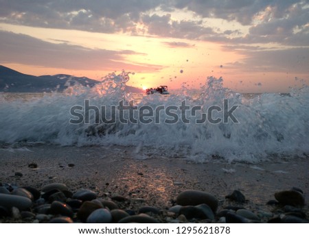 Sunset over the Adriatic sea with waves washing the shore on the foreground and a boat with tourists in the background, Vlora, Albania