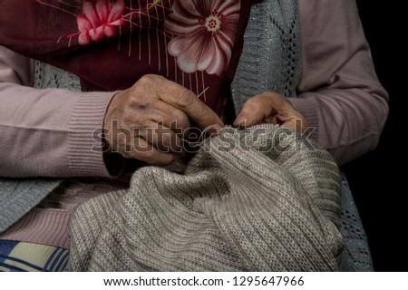 An old woman hands close-up knitting on knitting needles with black background.