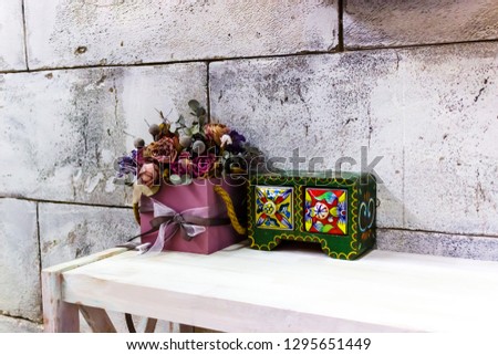 colorful boxes and flowers on the shelf on the background of concrete blocks and a mirror in which the Windows are reflected
