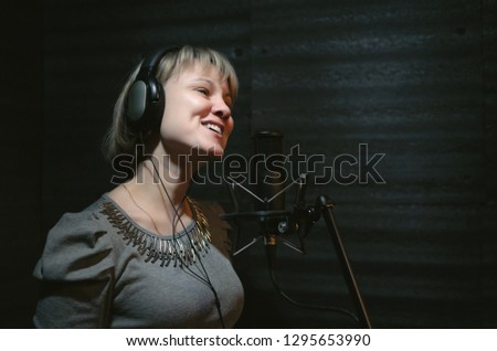 Woman a singer in a headphones is performing a song in a sound recording studio and is standing in front of the microphone.