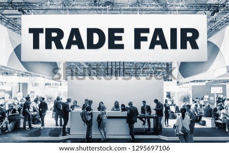 Crowd of people at a trade show booth with a banner and the text Trade Fair.
