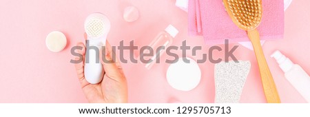 Bathroom accessories on a pastel pink background. Top view, copy space. Brush, loofah, towels, lotion, cream, pence. Face cleansing brush in hand