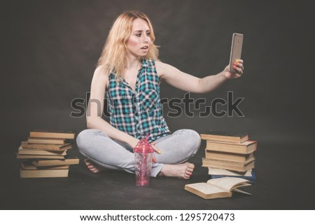 teen girl sitting on the floor next to books, does not want to learn, drinking juice and taking a selfie on the smartphone