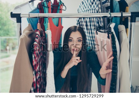 Portrait of nice attractive pretty charming cheerful cheery funny brunette girl lady hiding among clothes conspiracy in dressing room