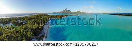 Aerial panoramic landscape view of the island of Bora Bora in French Polynesia with the Mont Otemanu mountain surrounded by a turquoise lagoon, motu atolls, reef barrier, and the South Pacific Ocean Royalty-Free Stock Photo #1295790217