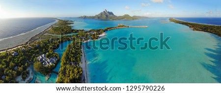 Aerial panoramic landscape view of the island of Bora Bora in French Polynesia with the Mont Otemanu mountain surrounded by a turquoise lagoon, motu atolls, reef barrier, and the South Pacific Ocean Royalty-Free Stock Photo #1295790226