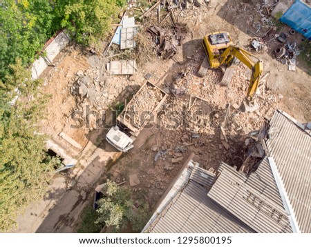 aerial view of demolition site with half ruined old building, yellow excavator and dumper truck