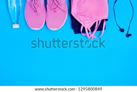 Flat lay a pair of sport shoes, earphones, bottle of water, leggings and sport crop top on a blue background. Concept healthy lifestyle, sport and diet. Top view.