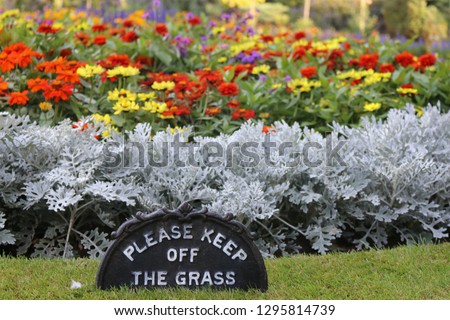 Please keep off the grass sign on a neatly edged grass lawn in front of a summer flower bedding display in a park.