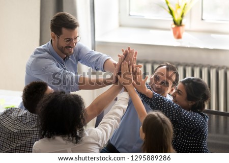 Successful millennial coworkers rises hands giving high five congratulating each other with great deal or goal achievement. Diverse multiracial business people feel happy received good news or reward Royalty-Free Stock Photo #1295889286