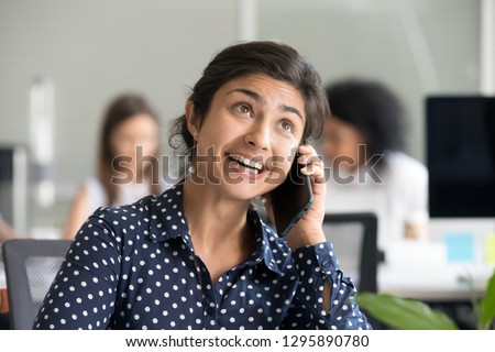 Head shot portrait indian female talking by smartphone. Happy hindu office worker has personal conversation sitting at desk in coworking space she knew great news received unbelievable opportunity Royalty-Free Stock Photo #1295890780