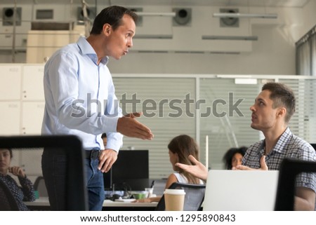 Angry millennial colleagues arguing in office workplace. Boss scolding incompetent employee discussing talking about mistake worker feels guilty justify self arguing explaining to director error cause Royalty-Free Stock Photo #1295890843