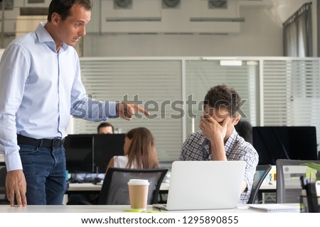 Angry dissatisfied boss ceo scolding employee in office. Frustrated office worker sitting at desk cover face with hand feels upset, director dismisses man for low poor result asking to leave workplace Royalty-Free Stock Photo #1295890855