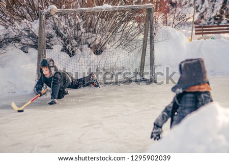 Two little boys in retro clothes are playing hockey on the handmade rink in Russia village. Image with selective focus, toning and noise effect.