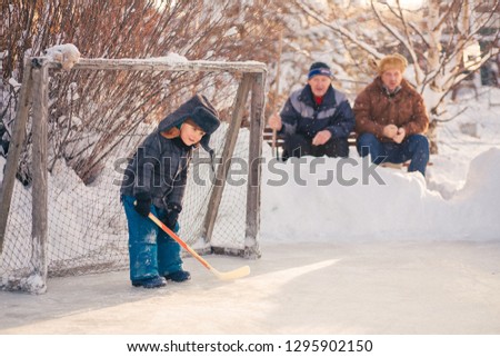 Two little boys in retro clothes are playing hockey in Russia. Two funny man are emotionly cheering for them. Image with selective focus, toning and noise effect.