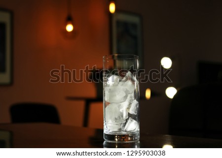 Glass with ice cubes on table in dark room