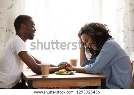 Happy smiling African American man on first date with attractive mixed race girlfriend in cafe, young couple in love laughing at funny joke together, drinking coffee, flirting, pleasant conversation Royalty-Free Stock Photo #1295925436